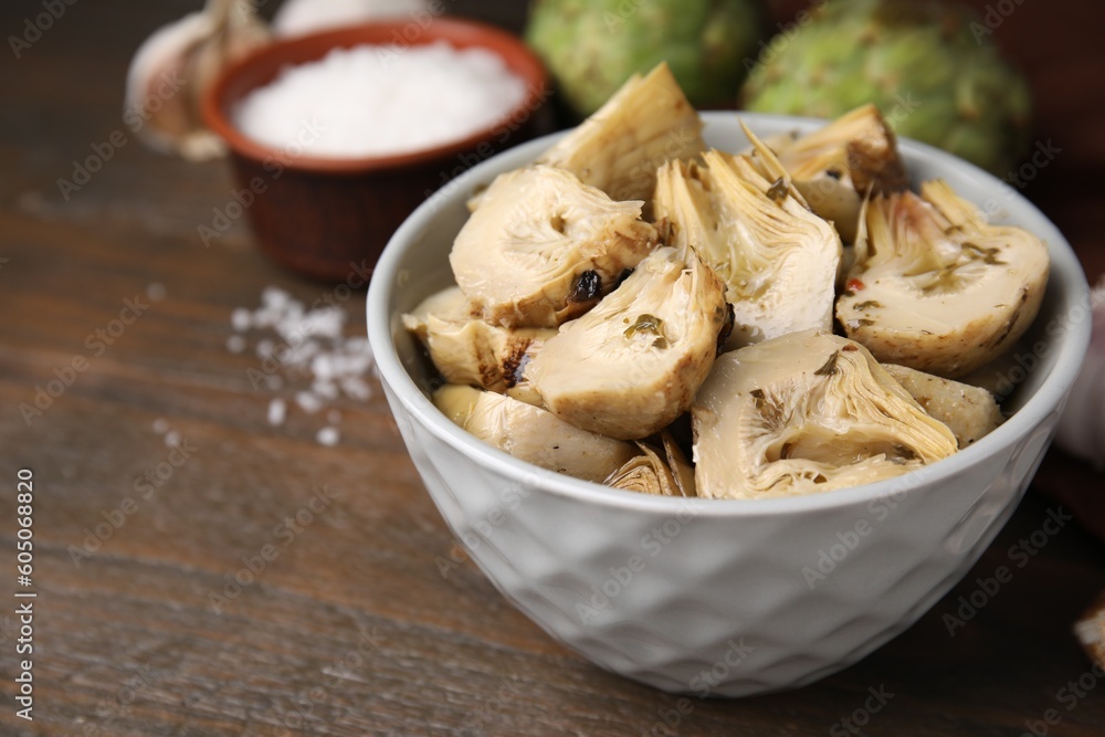 Bowl of pickled artichokes on wooden table, closeup