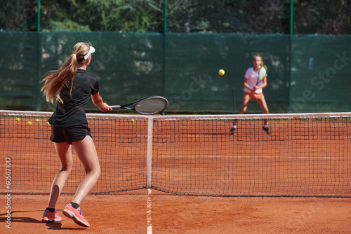 Young girls in a lively tennis match on a sunny day, demonstrating their skills and enthusiasm on a modern tennis court.