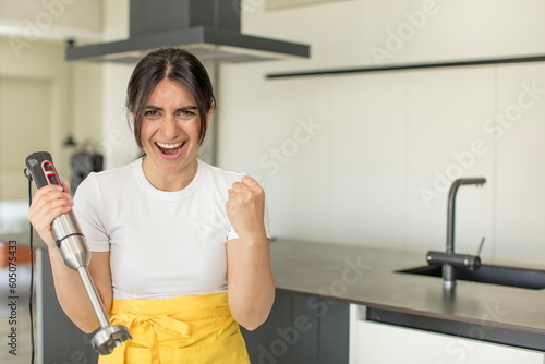 Fototapeta Naklejka Na Ścianę i Meble -  young woman looking angry, annoyed and frustrated. chef with hand blender