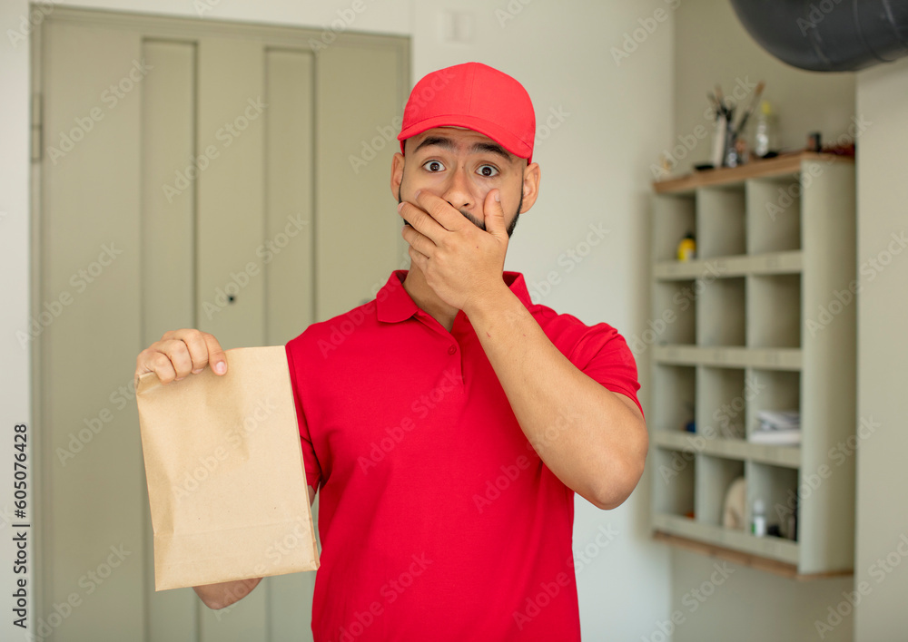 young adult man covering mouth with a hand and shocked or surprised expression. deliveryman concept young adult man covering mouth with a hand and shocked or surprised expression. deliveryman concept