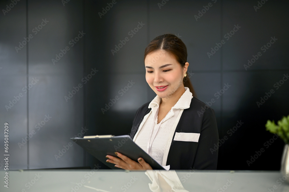 A beautiful Asian female receptionist reading and checking a document at front desk. A beautiful Asian female receptionist reading and checking a document at front desk.