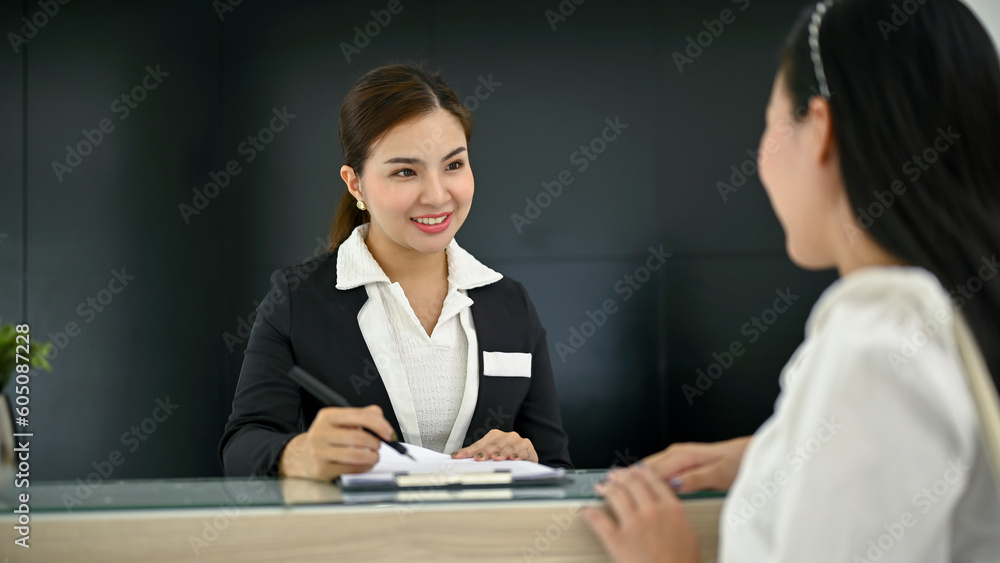 A beautiful Asian female receptionist is talking and asking for information from a customer A beautiful Asian female receptionist is talking and asking for information from a customer