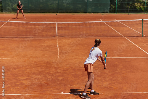 Young girls in a lively tennis match on a sunny day, demonstrating their skills and enthusiasm on a modern tennis court. © .shock