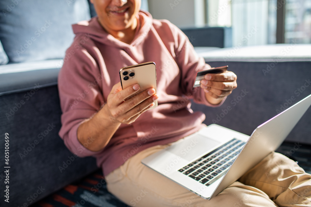 Middle aged latin man online shopping on his laptop and phone at home Middle aged latin man online shopping on his laptop and phone at home