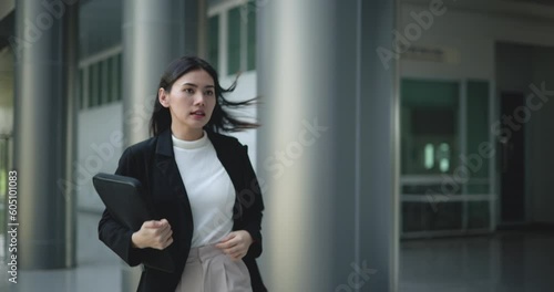 Footage of Young Asian businesswoman in suit holding a laptop and running in a hurry in a modern business building. Business and people concepts.