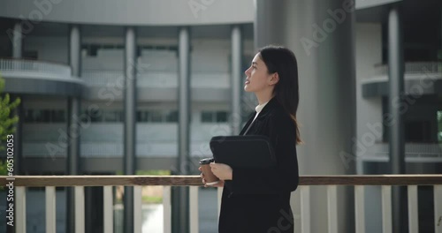 Side view shot, Footage of Happy young Asian businesswoman in suit holding a laptop and cup while walking in a modern business building. Business and people concepts.