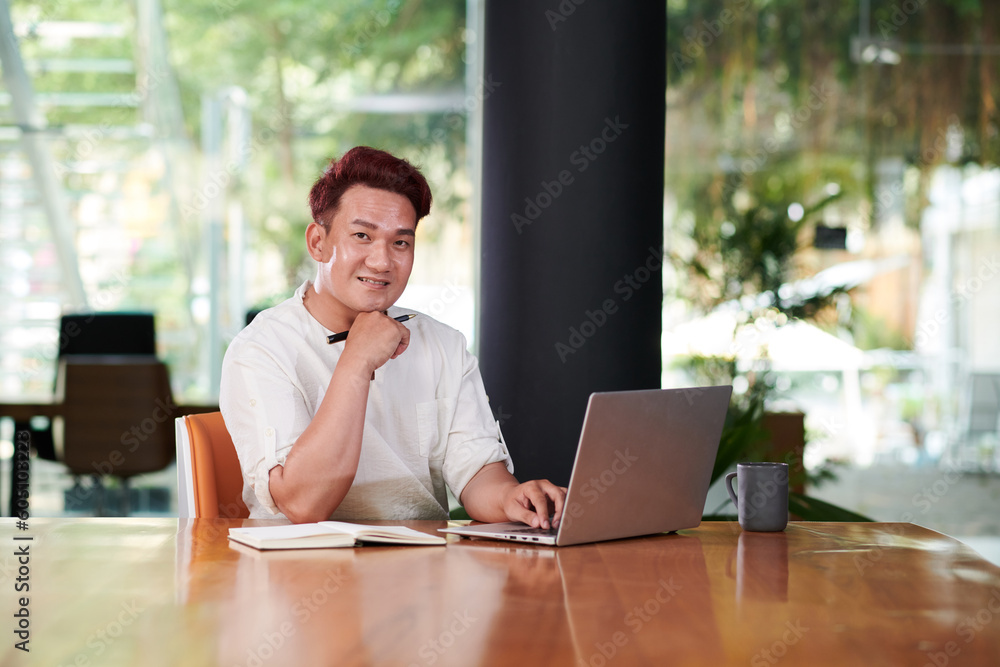 Confident smiling Asian businessman working on laptop in office Confident smiling Asian businessman working on laptop in office
