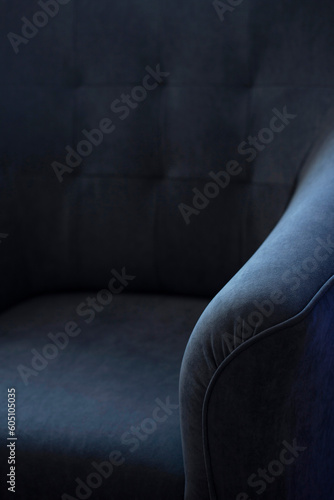 Upholstered furniture made of velor blue fabric with a curved element and a close-up carriage tie. Background of designer furniture in deep shadows with empty space for text. with copy space.