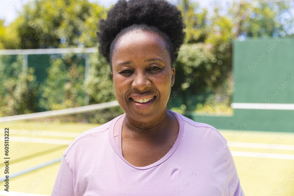 Portrait of happy senior african american woman on sunny grass tennis court Portrait of happy senior african american woman on sunny grass tennis court