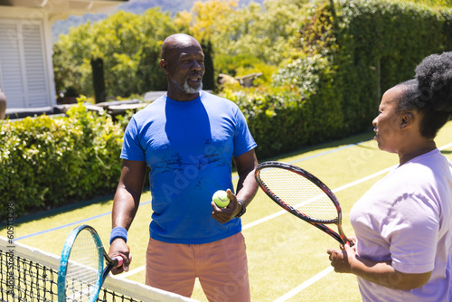Happy senior african american couple with tennis rackets talking on sunny grass court © wavebreak3