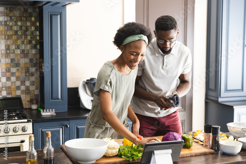 Happy african american couple preparing meal together using tablet in kitchen
