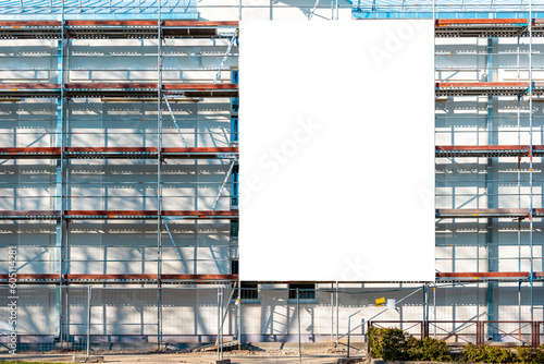 Blank white advertisement hanging on the scaffolding of modern building under construction.Reconstruction of a building with white billboard.