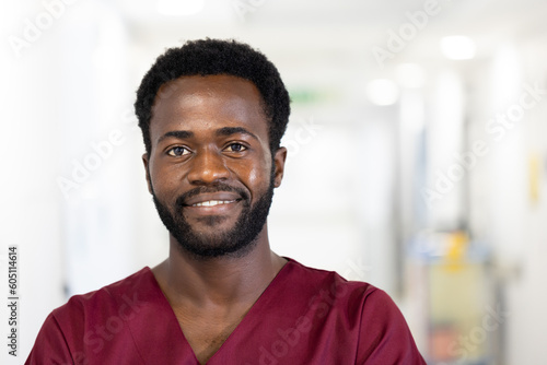 Unaltered portrait of african american male doctor in scrubs smiling, standing in hospital corridor