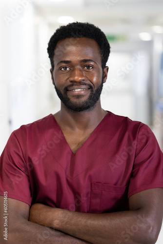 Unaltered portrait of african american male doctor in scrubs smiling, standing in hospital corridor