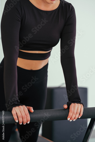 Unrecognizable woman wearing black sportswear practicing pilates exercises on reformer machine in studio.