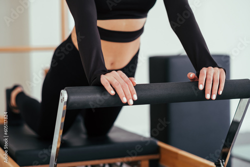 Unrecognizable woman wearing black sportswear practicing pilates exercises on reformer machine in studio.