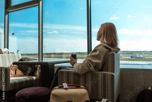 Travel.young woman at airport at window with suitcase waiting for plane, girl waiting for departure at the airport on your vacation. Uses a smartphone and drinks coffee