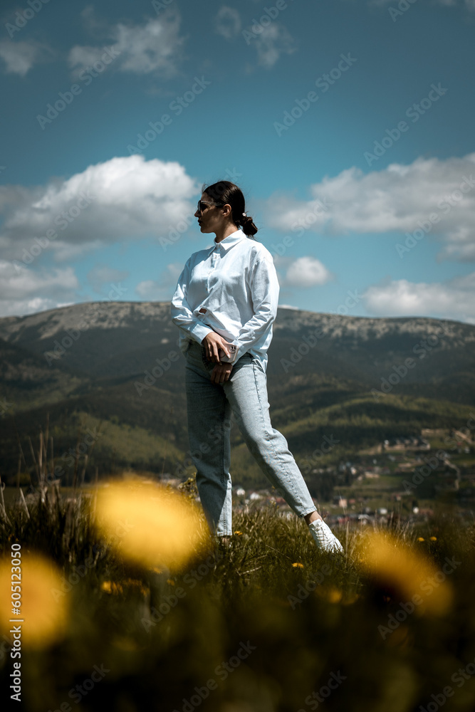 Stylish woman in a white shirt and glasses posing against the backdrop of mountains