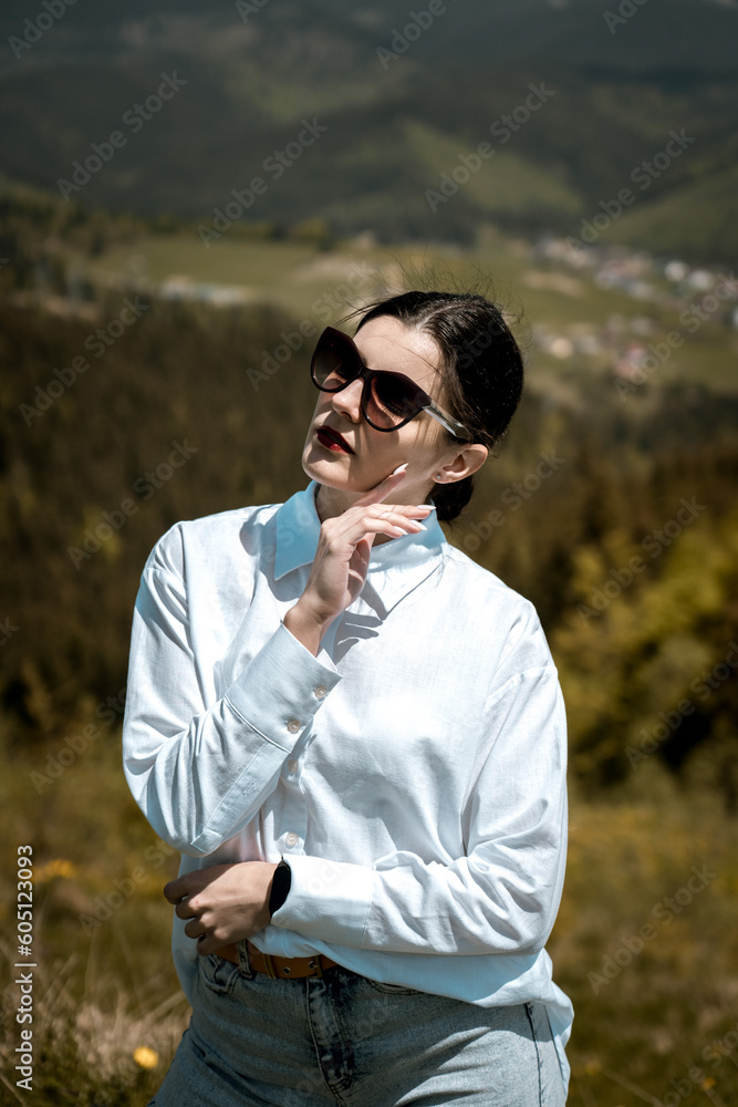 Stylish woman in a white shirt and glasses posing against the backdrop of mountains Stylish woman in a white shirt and glasses posing against the backdrop of mountains