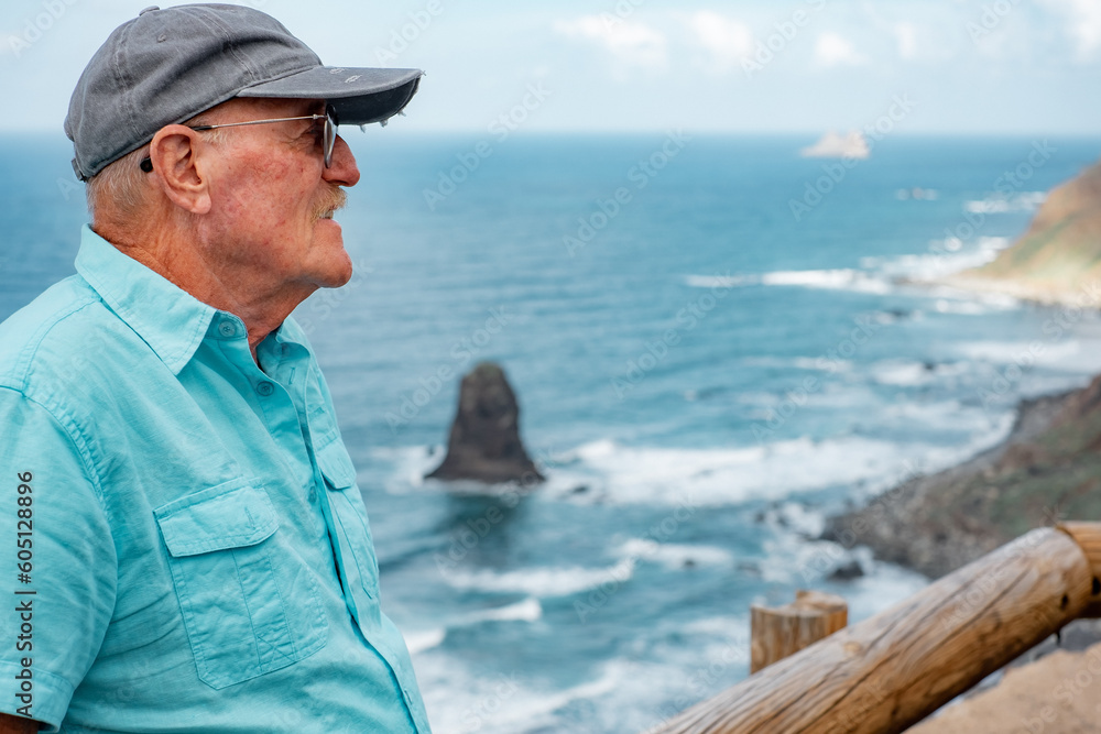 Portrait of alone senior man sitting close to the beach enjoying travel vacation and beauty in nature. Horizon over sea