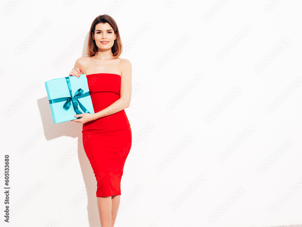 Young beautiful smiling female in red evening dress. Sexy brunette woman isolated. Positive model opens gift box, wondering whats inside as celebrating birthday. Receive b-day presents. Studio Young beautiful smiling female in red evening dress. Sexy brunette woman isolated. Positive model opens gift box, wondering whats inside as celebrating birthday. Receive b-day presents. Studio