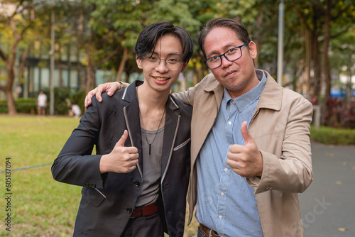 A older asian businessman in his 40s with his protege or son making a thumbs up sign at the park.