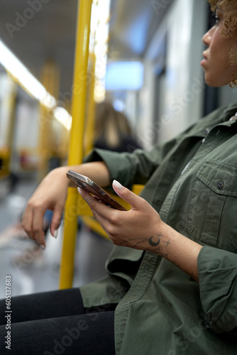 Vertical image of young afro woman traveling by underground and browsing a mobile phone