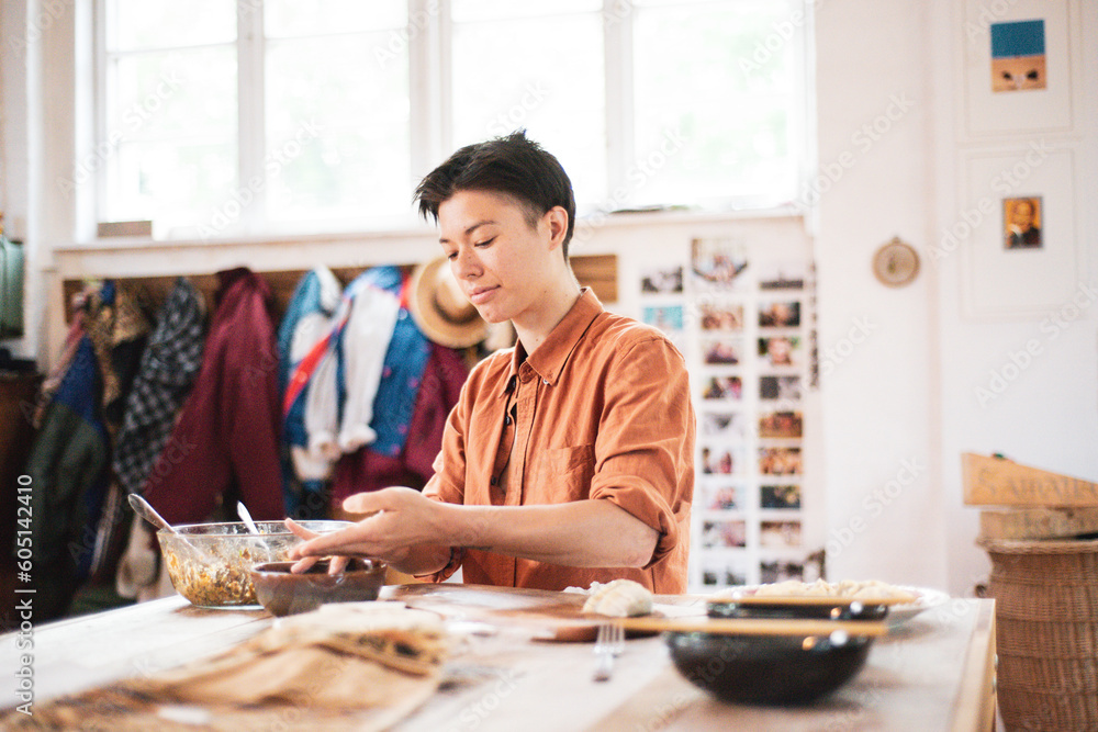 Androgynous asian prepares dumplings on wooden table at home Androgynous asian prepares dumplings on wooden table at home