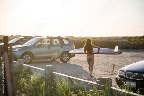 Woman in skimpy bikini walking with her surfboard at sunset
