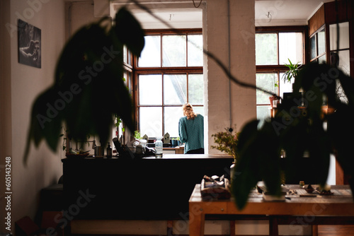 view through plants of woman in wooden kitchen cooking by window
