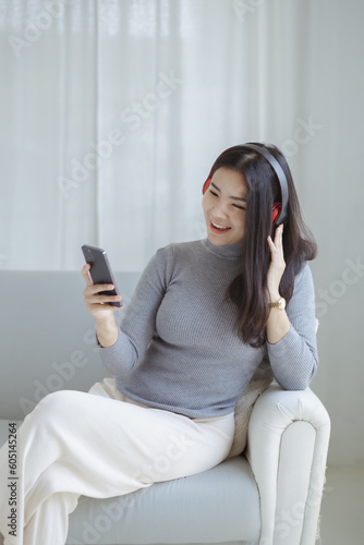 Asian woman dancing to the music playing from laptop on sofa in her home living room, weekend break, relaxation from hard work, drinking coffee. Take a vacation after a hard day's work.