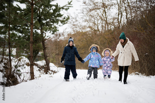 Mother with three kids holding hands and walking in winter forest.