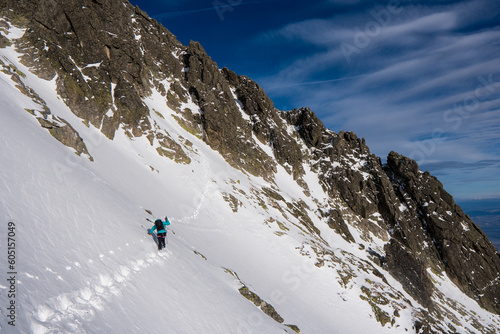 Adventurous women hiker a steep rocky cliff overlooking winter alpine like moutain landscape of High Tatras, Slovakia. Alpine mountain landscape covered with glaciers, snow and ice.	
