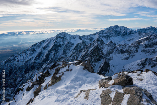 Fototapeta Naklejka Na Ścianę i Meble -  A Tourist standing on a mountain top above the clouds and looking at the view. Direct sunlight. Clear blue sky. Winter. Mountaineering. High Tatras mountain in Poland and Slovakia
