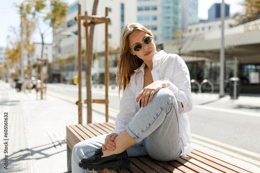 Candid attractive young smiling woman sitting on bench in Cyprus street wearing casual clothes, happy mood, fashion style trend
