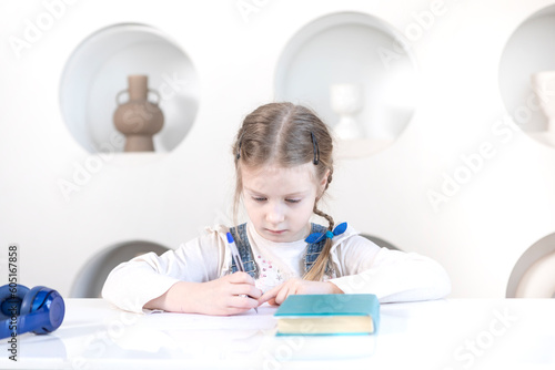Portrait of cute little girl in headphones sitting at the desk and studying at home. Preparation for school and homework concept