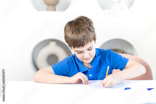 Cute happy school boy sits at the desk and learns his lessons	