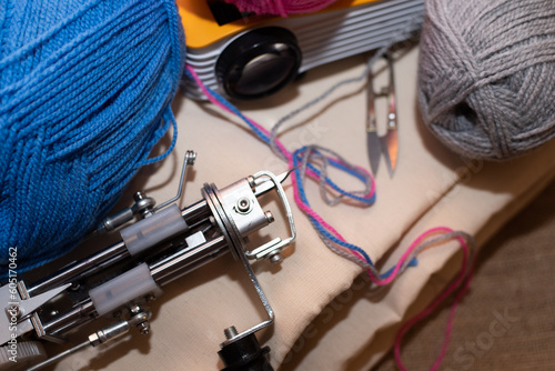 A tufting gun with multicolored yarns and drawing projector for drawing are laid on a sackcloth. Tufting kit.	
