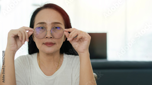 Portrait of focused adult Asian woman wearing eyeglasses on soft light from the window in livingroom