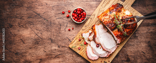 Baked pork loin on rustic wooden cutting board with spices, herbs and cranberries. Wood kitchen table background, top view banner with copy space