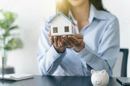 Businesswoman holding a house model.House on Hand with piggy bank.Real estate,Property insurance and security concept.Savings and finance concept.