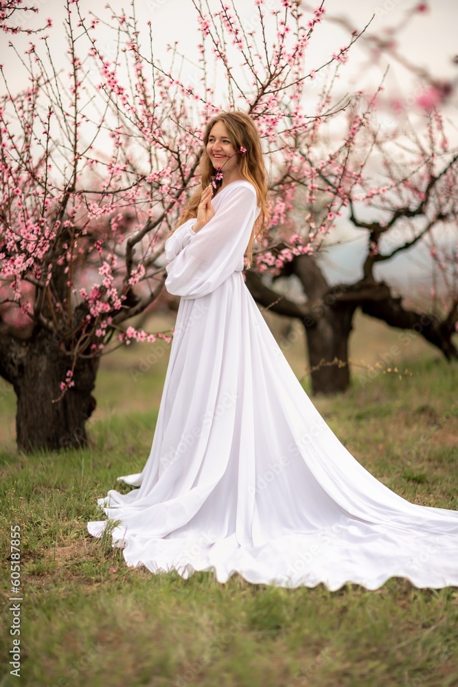 Woman peach blossom. Happy curly woman in white dress walking in the garden of blossoming peach trees in spring