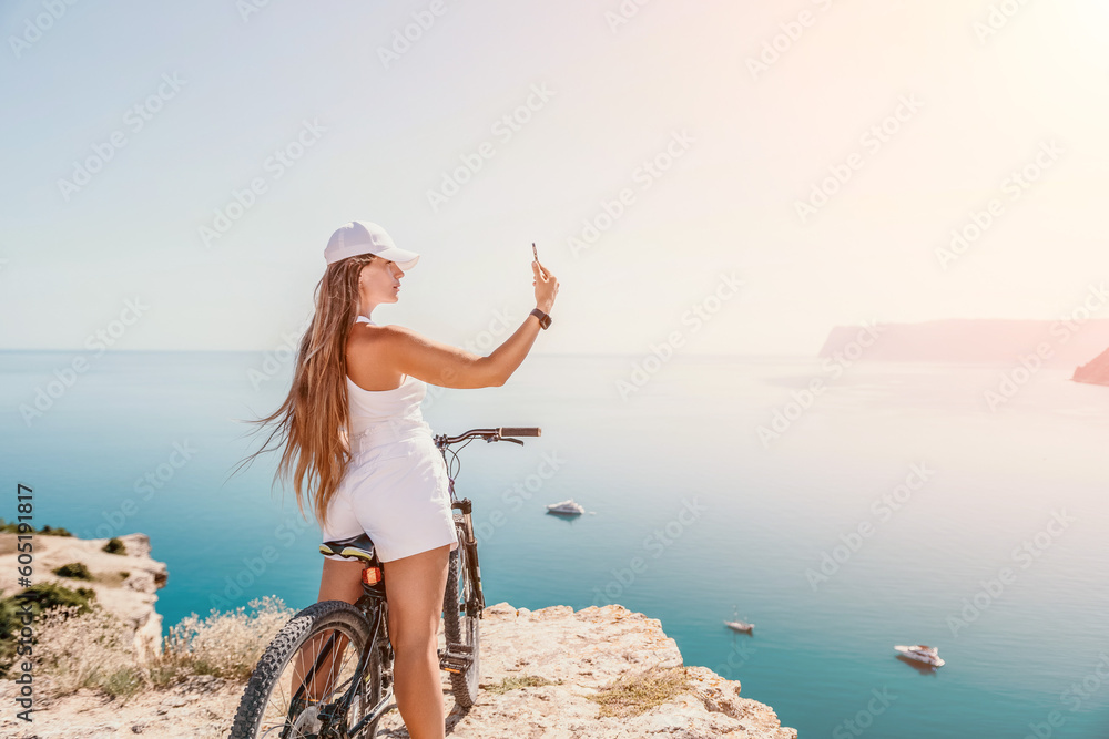 A woman cyclist on a mountain bike looking at the landscape of mountains and sea. Rear view of cyclist woman standing in front to the sea with outstretched arms. Freedom and healthy lifestyle concept. A woman cyclist on a mountain bike looking at the landscape of mountains and sea. Rear view of cyclist woman standing in front to the sea with outstretched arms. Freedom and healthy lifestyle concept.