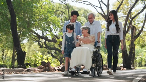Happy Asian senior woman sitting on wheelchair in the park and take care by big family on weekends holiday