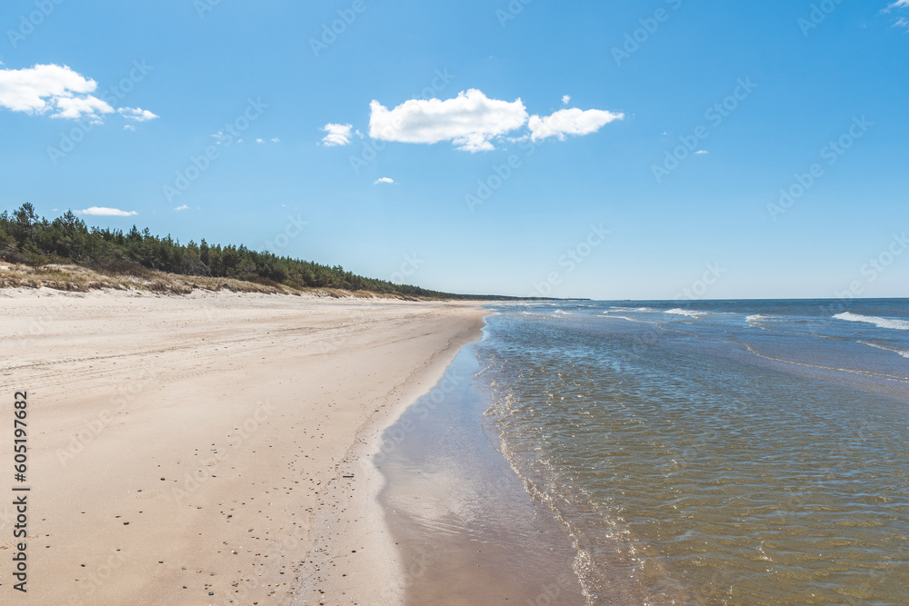 Walking on the Baltic Sea in Palanga, Klaipeda, Lithuania, with waves, cloudy sky, white sandy beach and dunes with reeds and pine tree forest