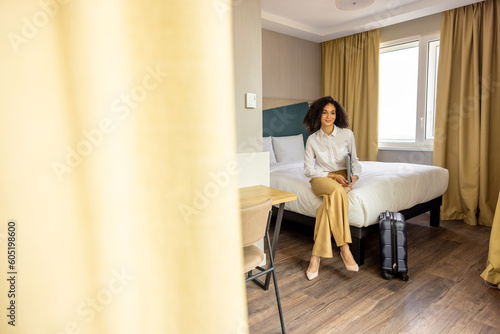 In hotel room. Smiling young woman with the laptop sitting on bed