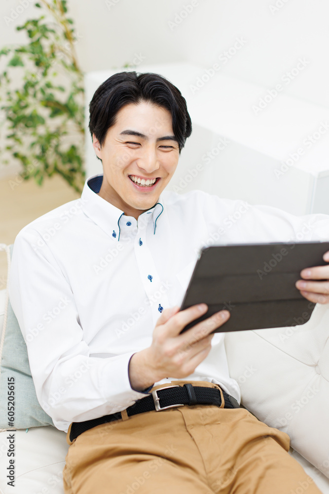 微笑んで、ソファでデジタルタブレットを使用する日本人男性