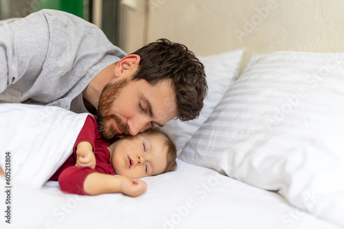 Handsome brunette father kissing sleeping infant baby tenderly.