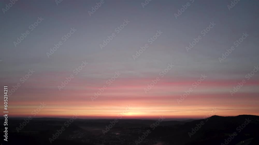 Drone shot showing a beautiful orange-glowing sunrise in the morning, tilting down to reveal a small village with low-hanging clouds located next to a highway Drone shot showing a beautiful orange-glowing sunrise in the morning, tilting down to reveal a small village with low-hanging clouds located next to a highway