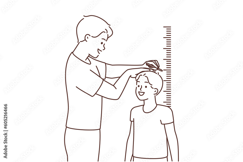 Smiling father measure son height near wall 